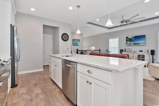 kitchen featuring white cabinets, appliances with stainless steel finishes, open floor plan, light wood-style floors, and a sink