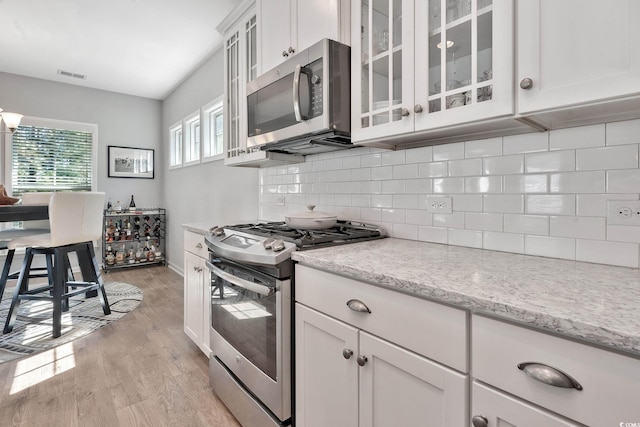 kitchen with visible vents, backsplash, appliances with stainless steel finishes, white cabinets, and light wood-type flooring