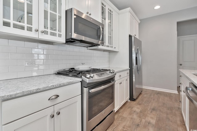 kitchen featuring light wood-style flooring, stainless steel appliances, white cabinetry, baseboards, and decorative backsplash