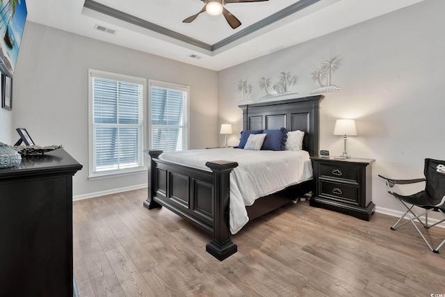 bedroom featuring light wood-style floors, a tray ceiling, visible vents, and baseboards