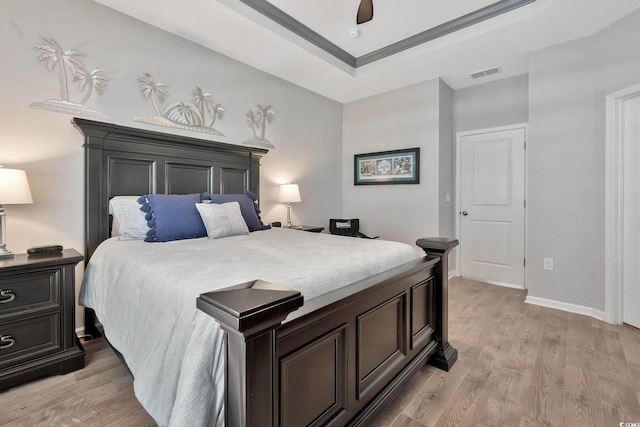 bedroom featuring light wood-style flooring, a raised ceiling, visible vents, and baseboards