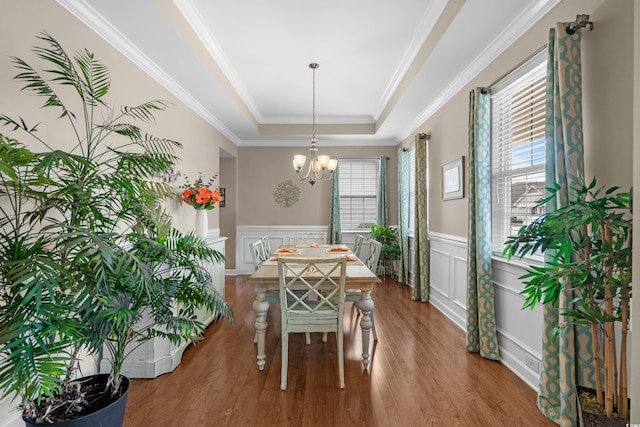 dining room featuring a notable chandelier, a raised ceiling, ornamental molding, wainscoting, and wood finished floors