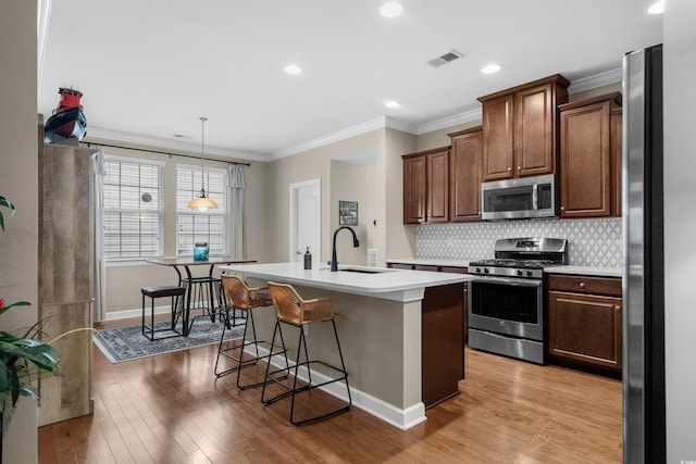 kitchen with stainless steel appliances, a sink, visible vents, light countertops, and light wood finished floors