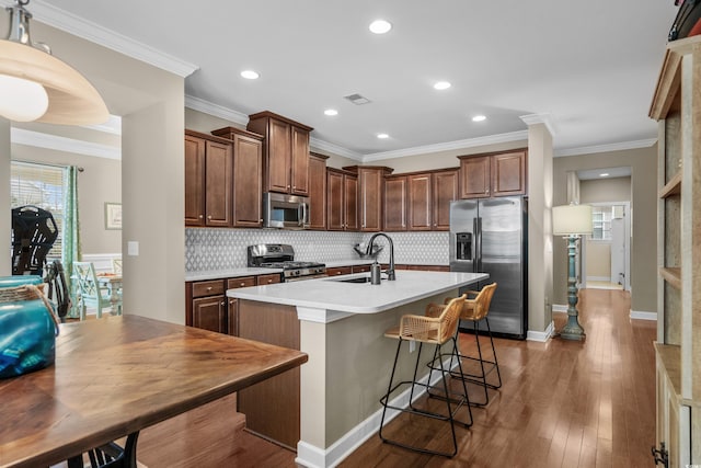 kitchen with a sink, backsplash, appliances with stainless steel finishes, a center island with sink, and dark wood-style floors