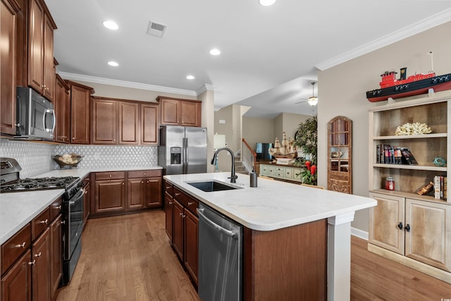 kitchen with crown molding, stainless steel appliances, a center island with sink, a sink, and visible vents
