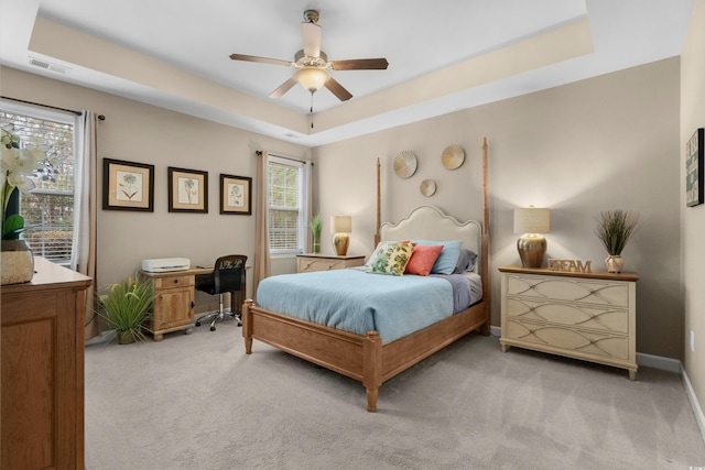 bedroom with baseboards, visible vents, light colored carpet, ceiling fan, and a tray ceiling