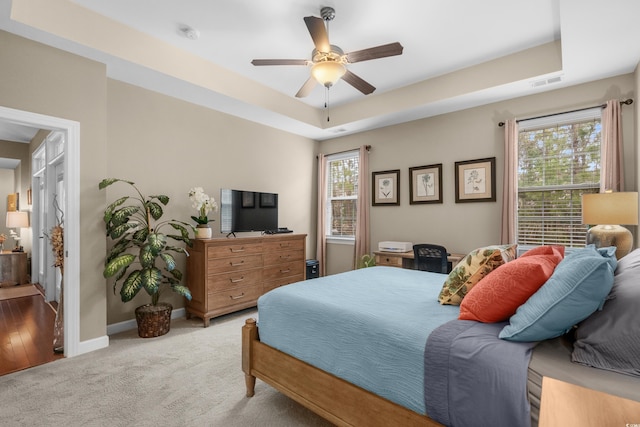 carpeted bedroom with baseboards, a tray ceiling, visible vents, and multiple windows