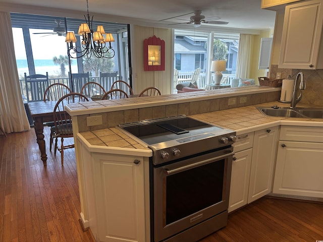 kitchen with dark wood-style flooring, a sink, tile counters, and stainless steel range with electric cooktop