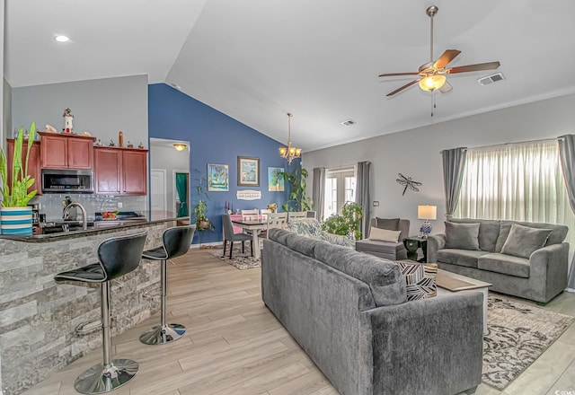 living room featuring visible vents, ceiling fan with notable chandelier, lofted ceiling, and light wood finished floors