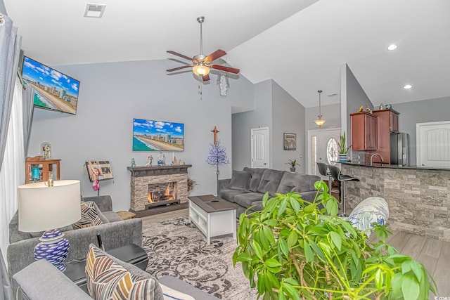 living area featuring visible vents, ceiling fan, a fireplace, wood finished floors, and high vaulted ceiling