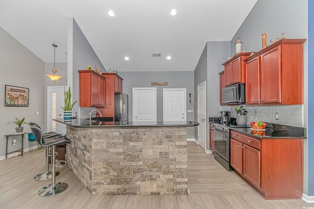 kitchen featuring stainless steel appliances, a kitchen bar, dark countertops, and a peninsula