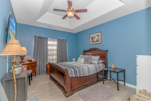 bedroom with visible vents, baseboards, light wood finished floors, ceiling fan, and a raised ceiling