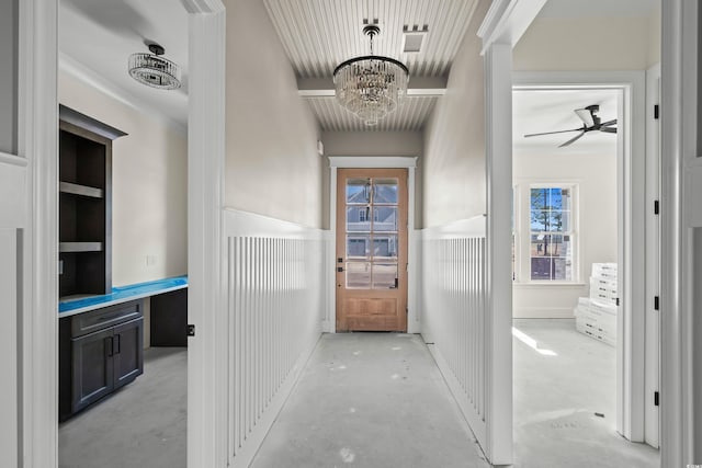 hall with a wainscoted wall, plenty of natural light, a chandelier, and concrete flooring