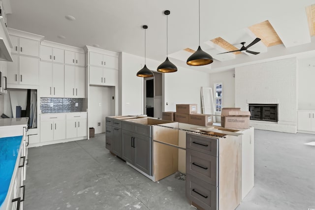 kitchen featuring a center island, tasteful backsplash, a brick fireplace, white cabinets, and concrete flooring