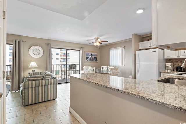 kitchen featuring light stone countertops, white cabinetry, a ceiling fan, and freestanding refrigerator