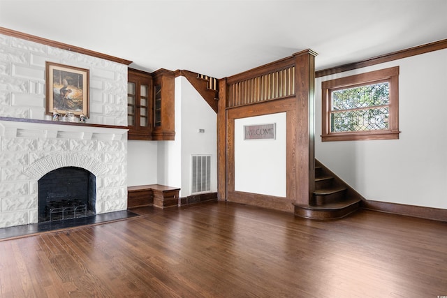 unfurnished living room with a fireplace, wood finished floors, visible vents, baseboards, and stairway