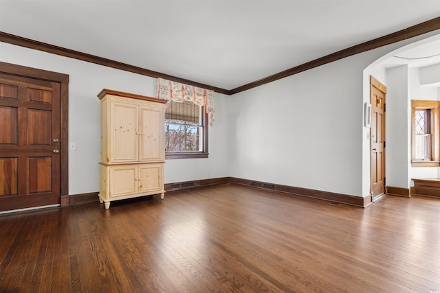 spare room with arched walkways, dark wood-style flooring, visible vents, baseboards, and ornamental molding