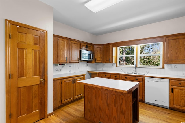 kitchen with a sink, light countertops, light wood-type flooring, dishwasher, and stainless steel microwave