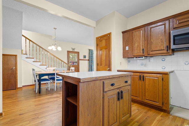 kitchen with light wood finished floors, stainless steel microwave, light countertops, and decorative backsplash