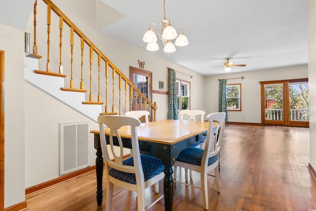 dining area featuring ceiling fan with notable chandelier, wood finished floors, visible vents, baseboards, and stairway