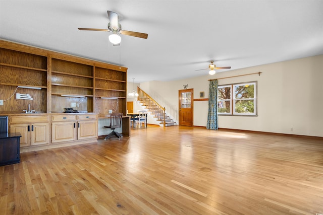 unfurnished living room with ceiling fan, built in desk, a sink, and light wood-style floors