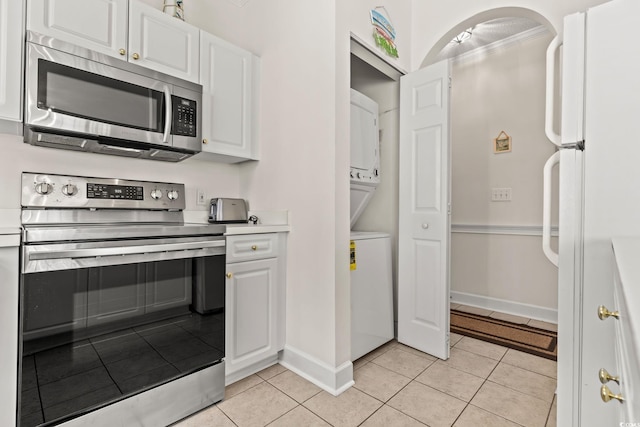 kitchen featuring light tile patterned floors, stainless steel appliances, light countertops, stacked washer / drying machine, and white cabinetry