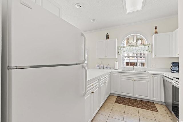 kitchen with light tile patterned flooring, freestanding refrigerator, a sink, light countertops, and white cabinetry