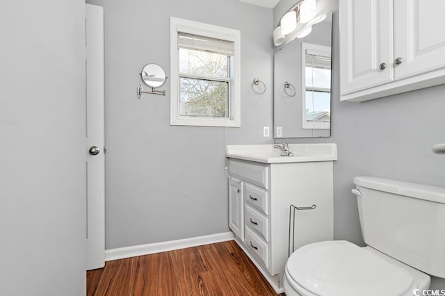 half bath featuring baseboards, vanity, toilet, and wood finished floors