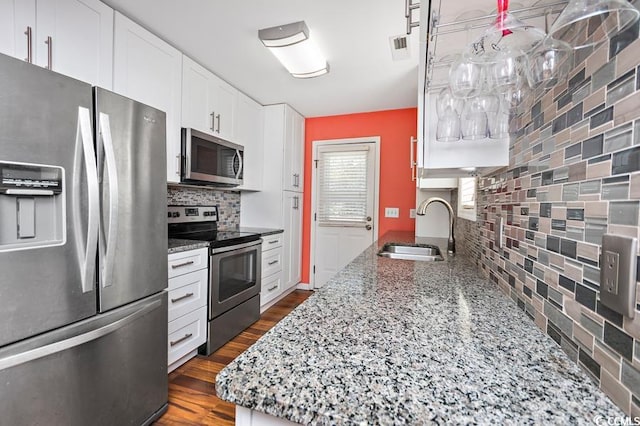 kitchen featuring stone counters, dark wood-style floors, backsplash, appliances with stainless steel finishes, and a sink