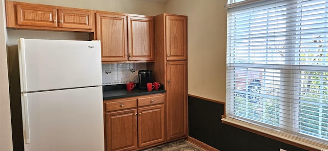 kitchen featuring tasteful backsplash, brown cabinetry, dark countertops, and freestanding refrigerator