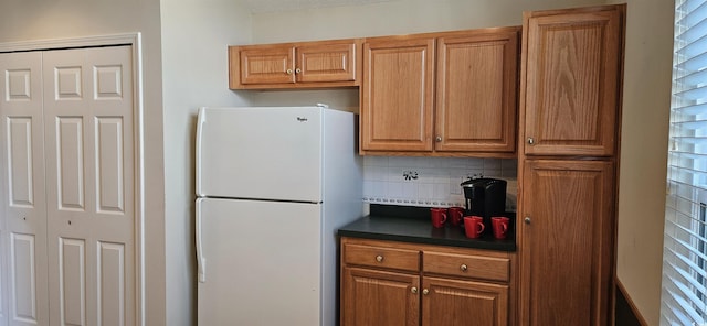 kitchen featuring dark countertops, tasteful backsplash, brown cabinetry, and freestanding refrigerator