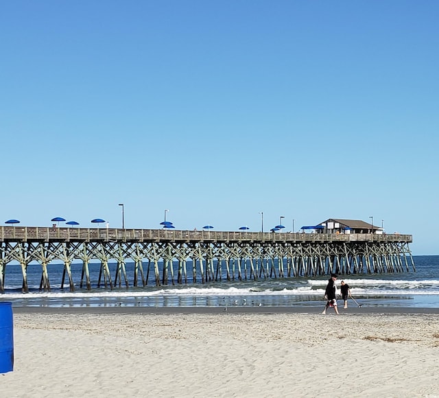 surrounding community featuring a pier, a water view, and a view of the beach