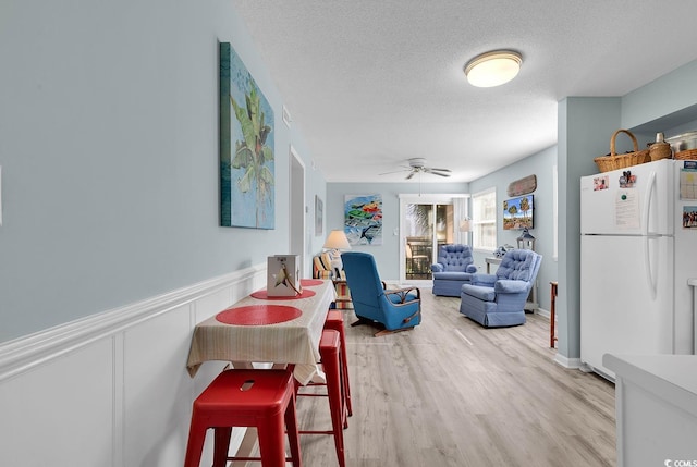 dining area featuring light wood-style floors, a textured ceiling, wainscoting, and a ceiling fan