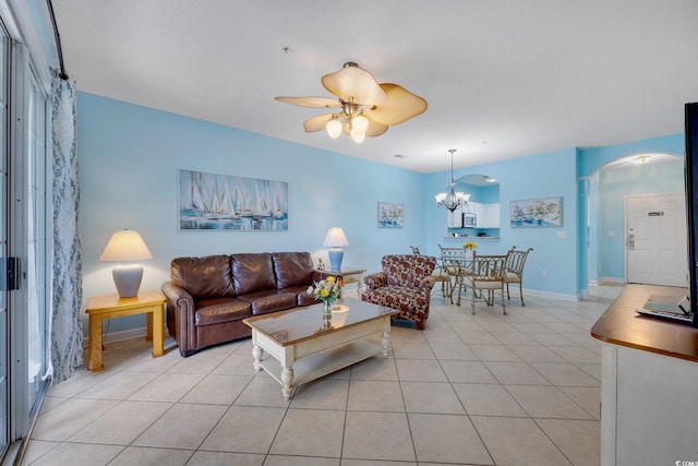 living area featuring ceiling fan with notable chandelier, arched walkways, baseboards, and light tile patterned floors