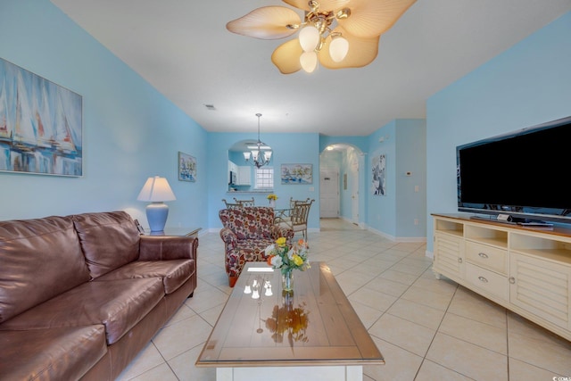 living area with light tile patterned floors, baseboards, arched walkways, and ceiling fan with notable chandelier