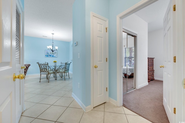 hall featuring light tile patterned floors, light carpet, baseboards, and a notable chandelier