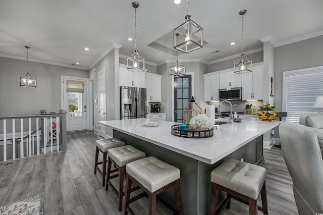 kitchen with white cabinets, appliances with stainless steel finishes, a kitchen breakfast bar, wood finished floors, and a sink