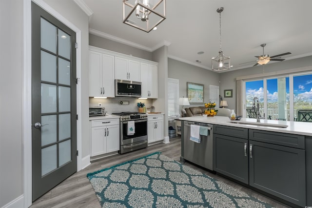 kitchen featuring appliances with stainless steel finishes, light countertops, crown molding, white cabinetry, and a sink