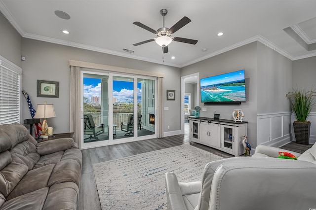 living area with ornamental molding, wood finished floors, visible vents, and a ceiling fan