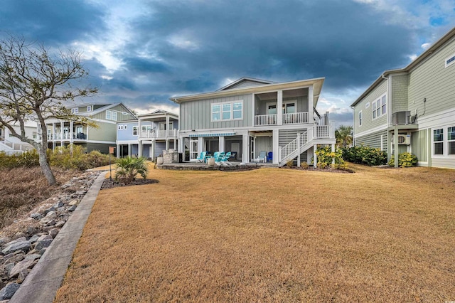 rear view of property featuring board and batten siding, stairs, a yard, and a patio