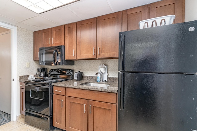 kitchen with light stone countertops, black appliances, brown cabinetry, and a sink