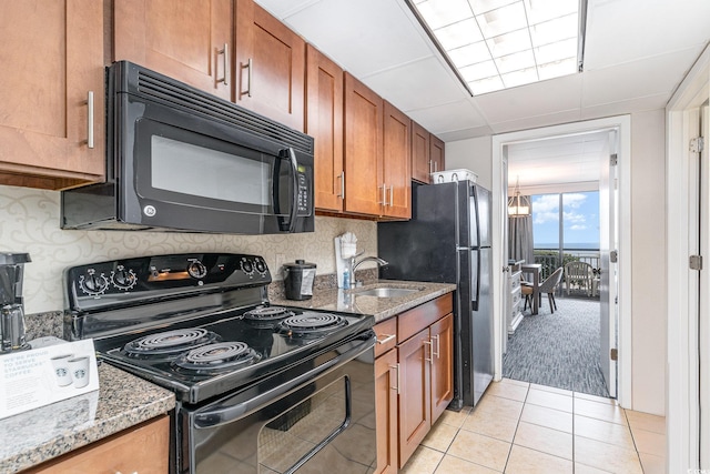 kitchen with light tile patterned floors, a sink, black appliances, tasteful backsplash, and brown cabinetry