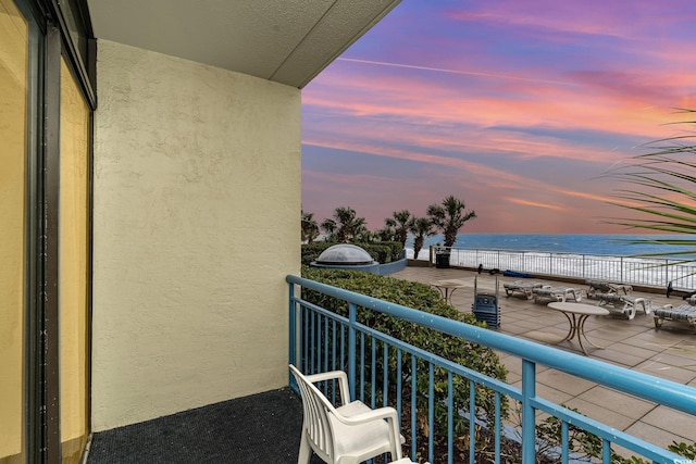 balcony at dusk featuring a water view and a view of the beach