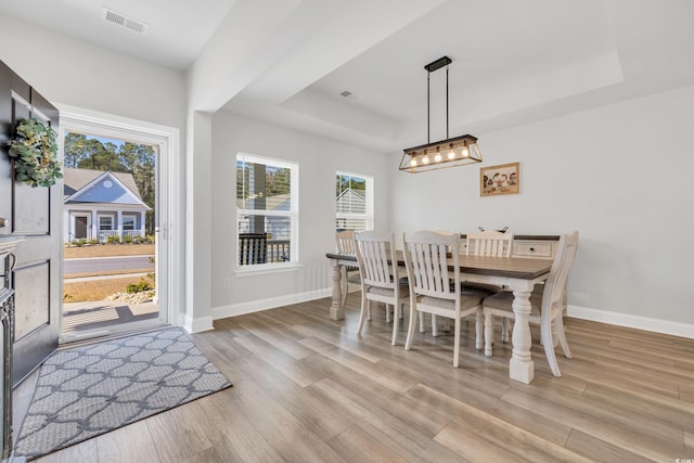 dining space featuring light wood-type flooring, a raised ceiling, visible vents, and baseboards