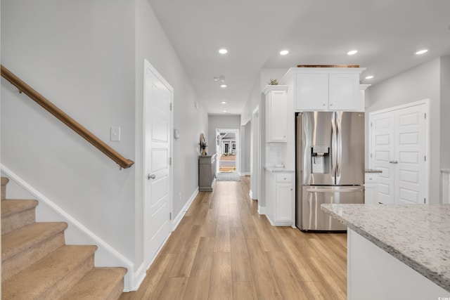 kitchen with light wood finished floors, stainless steel fridge, light stone counters, white cabinetry, and recessed lighting