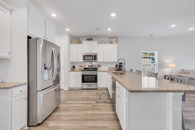 kitchen featuring stainless steel appliances, recessed lighting, light wood-style flooring, a sink, and a peninsula