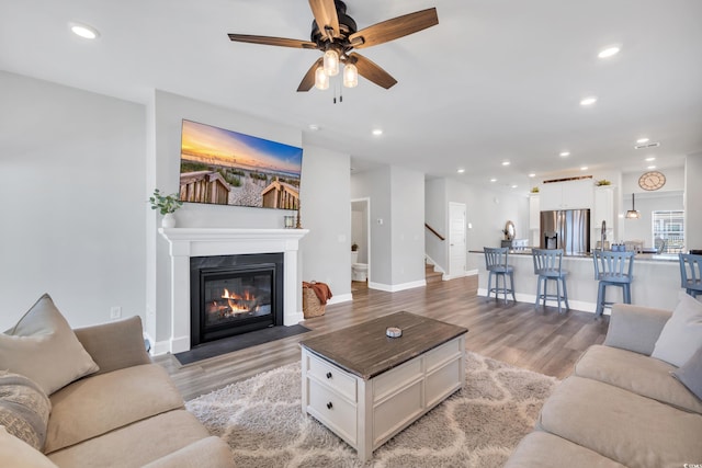 living area with baseboards, a fireplace with flush hearth, stairway, light wood-style floors, and recessed lighting