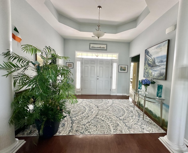 foyer with wood finished floors, a raised ceiling, and ornate columns