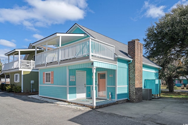 view of front of house with a shingled roof, a chimney, cooling unit, and a balcony