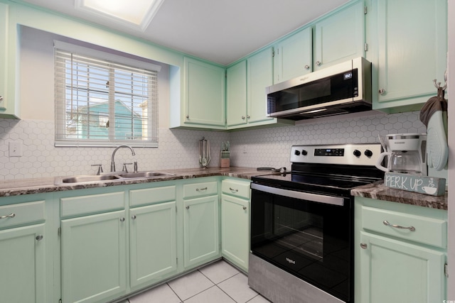 kitchen featuring green cabinets, light tile patterned floors, stainless steel appliances, and a sink